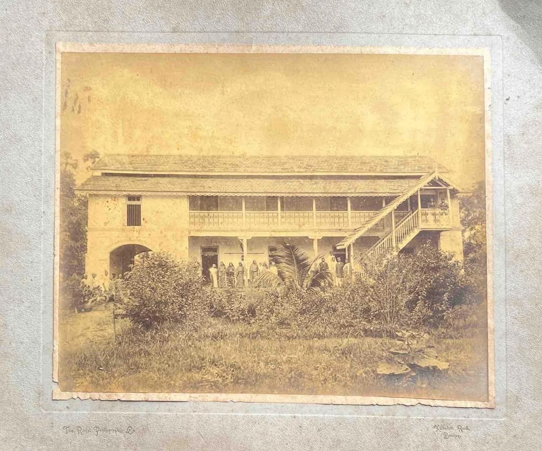 COLONIAL-ERA HOUSE WITH VERANDAH AND GARDEN: COLONIAL-ERA HOUSE WITH VERANDAH AND GARDEN THE IMAGE SHOWS AN OLD, TWO-STOREY COLONIAL-STYLE BUILDING WITH A LONG VERANDAH RUNNING ACROSS THE UPPER FLOOR. A WOODEN STAIRWAY ON THE RIGHT SIDE LEADS TO