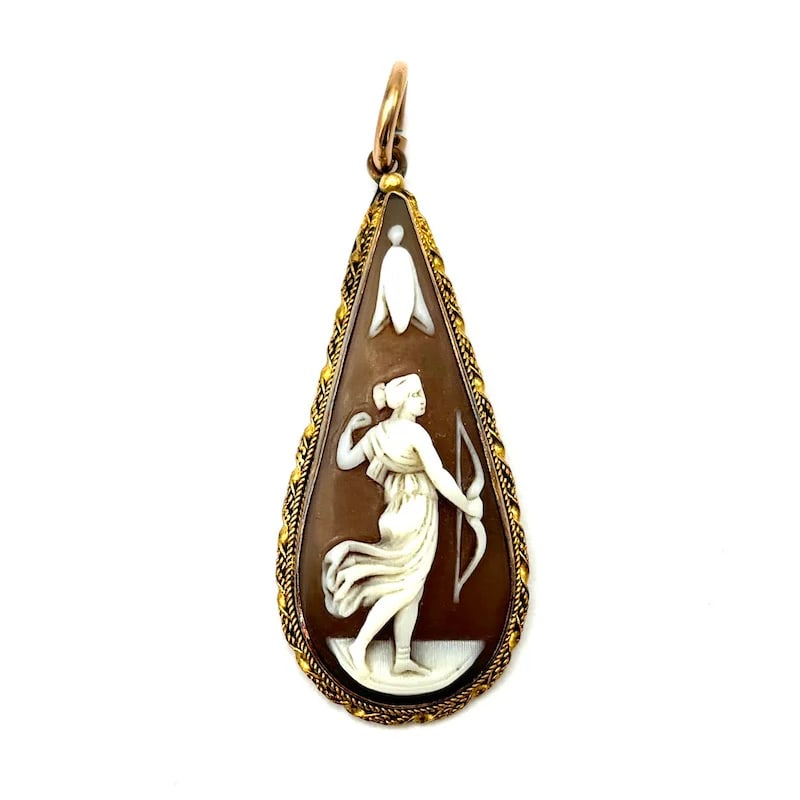 Late 1800s 18K Yellow Gold Pendant with Female Hunter portrait carved on Sardonyx Shell, 3.67 gr: An antique pendant crafted in 18K yellow gold, featuring an intricately carved sardonyx shell relief portraying a noble female hunter in motion. Shaped in a graceful drop silhouette and framed by a tw