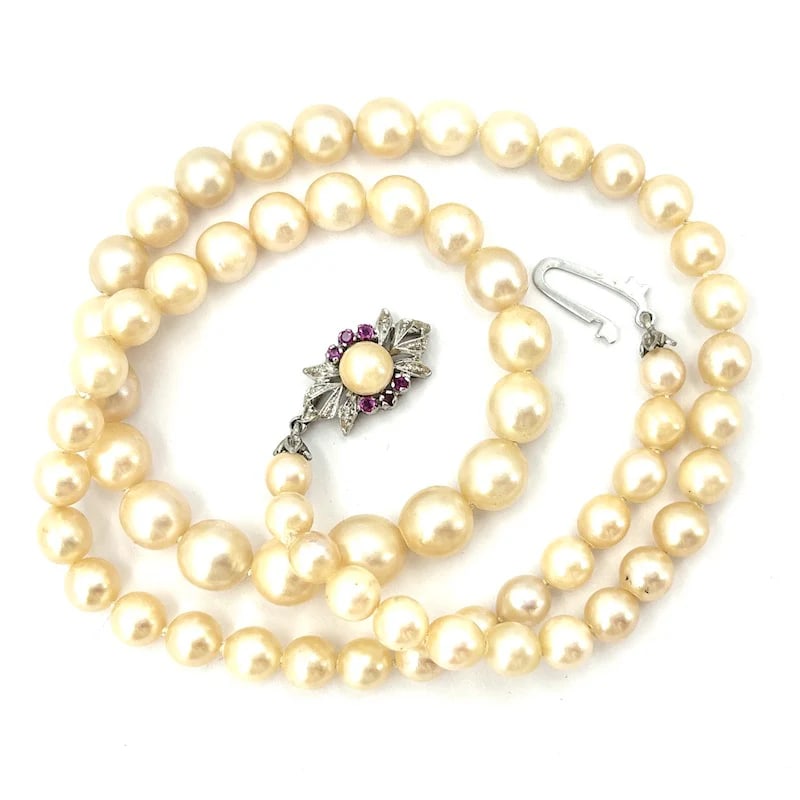 Graduated Akoya Pearl Necklace with Central Pearl and White Gold 18k Clasp, Ruby Accents, 36.01 gr: Beautiful necklace featuring a graduated strand of natural Akoya pearls, each uniquely irregular, with a central pearl, finished with a stylish 18k white gold clasp adorned with ruby accents. Weight: