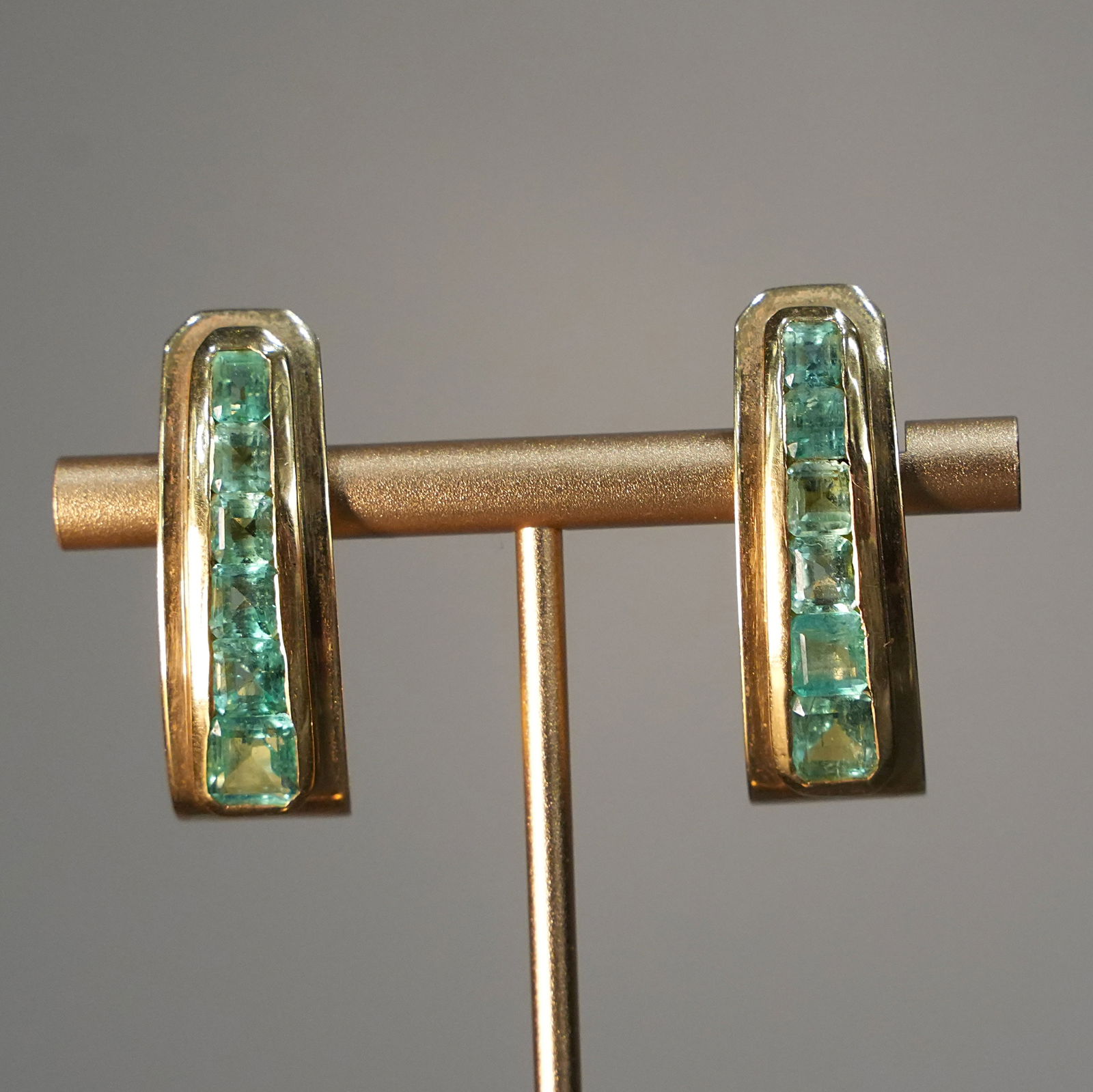 Art Deco 18K Yellow Gold Clip Earrings with Colombian Emeralds in Geometric Shield Design, 15.85gr: 18K yellow gold clip earrings inspired by Art Deco geometry, featuring a sleek shield-shaped silhouette that frames the face with refined elegance. Each earring showcases a vertical row of natural squ