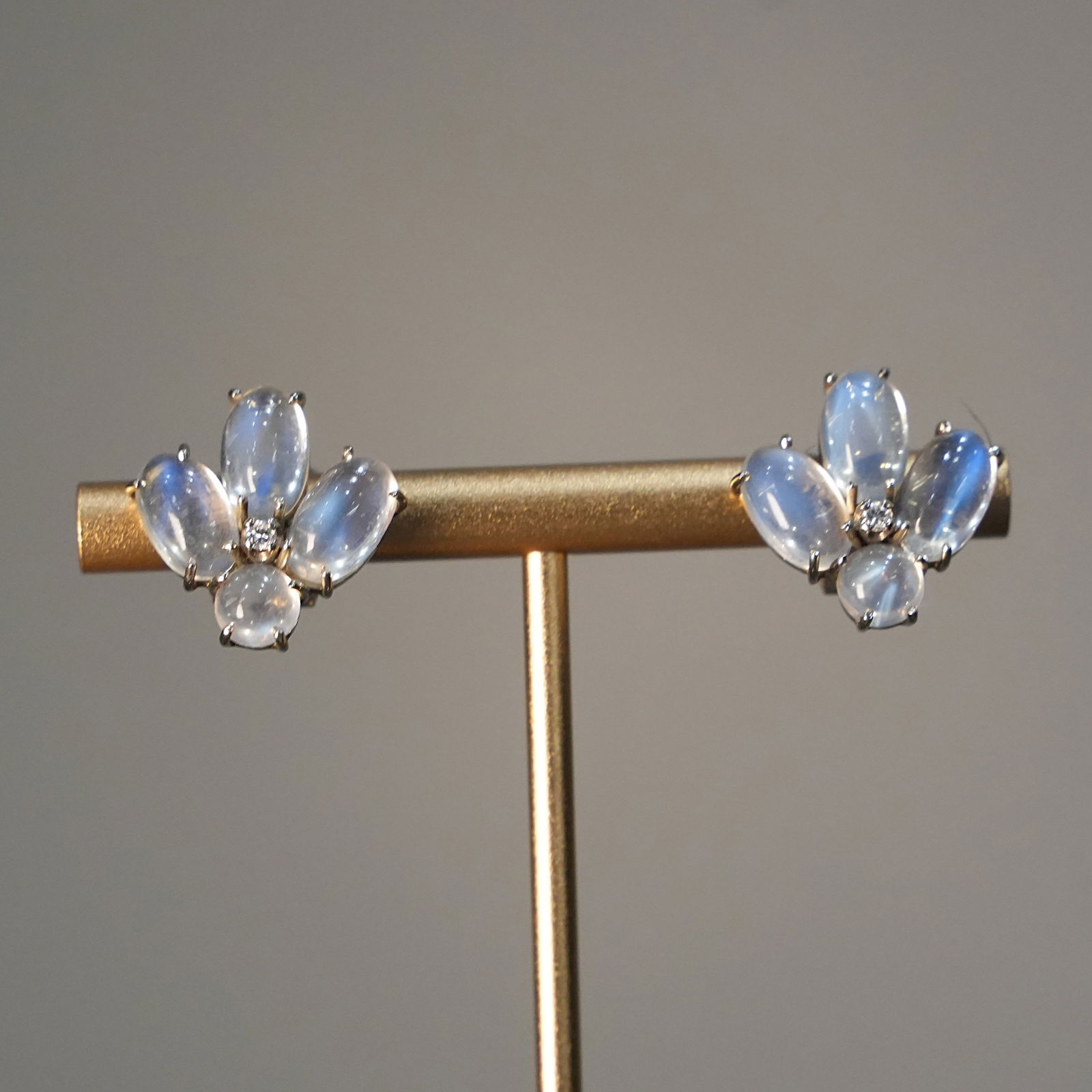 Bouquet-Inspired Moonstone Clip Earrings in 18K White Gold and 2 Diamonds 0.10 ct total, 6.91 gr: Refined clip earrings crafted in solid 18K white gold, featuring a sculpted bouquet-inspired silhouette. The fan-shaped arrangement highlights luminous moonstones with soft bluish reflections, while a