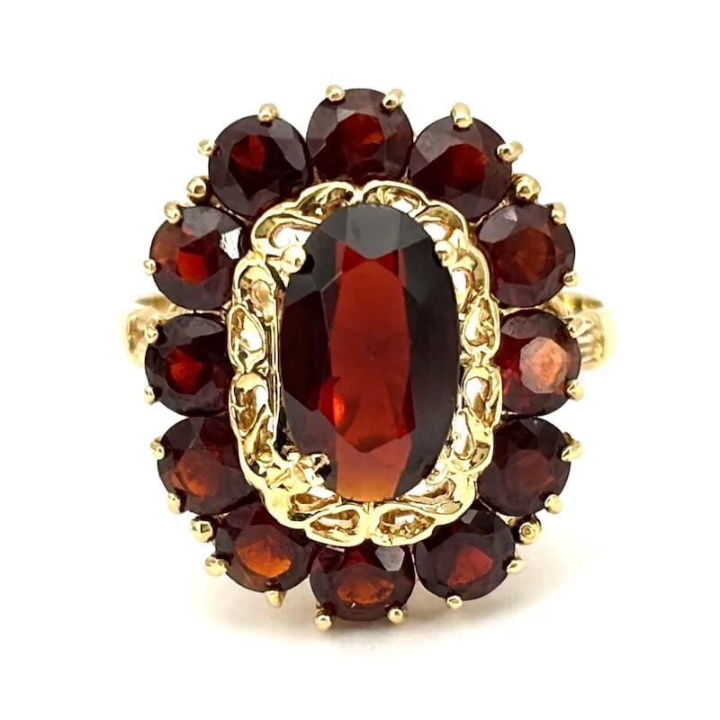 Vintage oval panel ring in 18kt yellow gold with garnets and intricate openwork design, 4.64gr: Refined vintage panel ring crafted in 18kt yellow gold, featuring an oval openwork surface with a framed arrangement of garnets, expressing artisanal detail and a distinctive old-world character throu