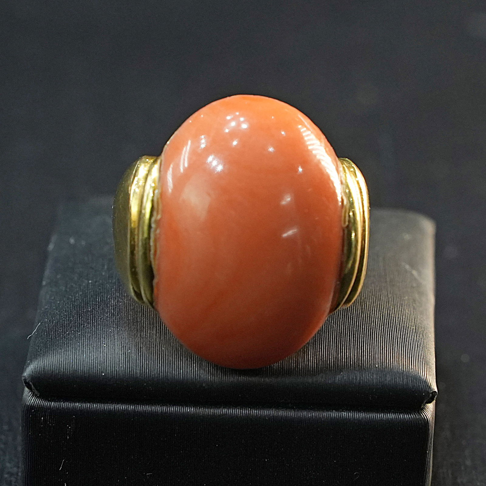 A Distinctive Yellow 18K Gold Ring Featuring Prominent Oval Cabochon Coral, Elegant Design, 14.50gr: A Distinctive 18K yellow gold ring showcasing a bold oval cabochon coral centerpiece. The polished gold band highlights the vibrant coral, creating a refined and eye-catching statement piece for any c