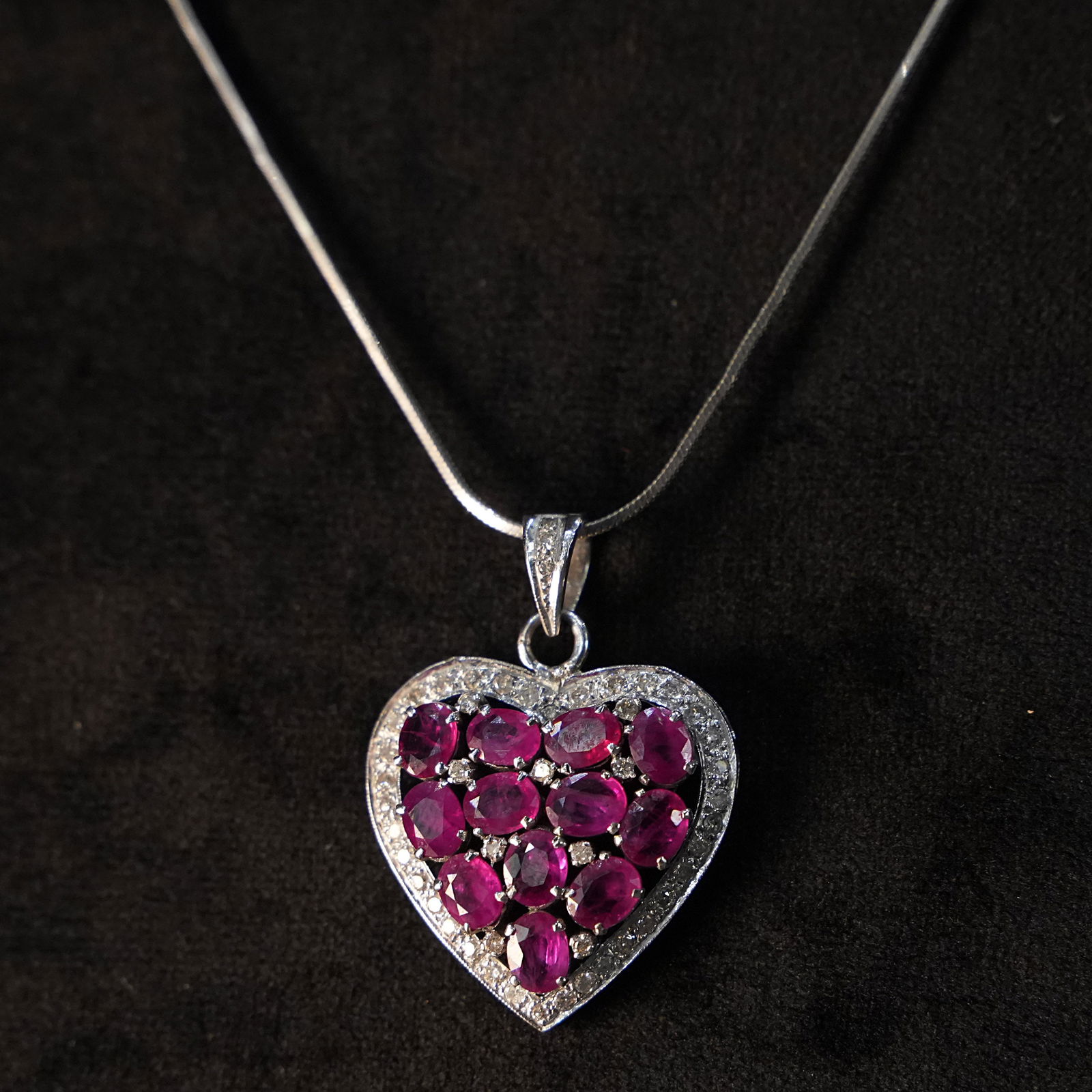 Romantic 18K White Gold Pendant with Ruby Heart Surrounded by Diamonds 5.94gr: A romantic pendant crafted in 18K white gold, featuring a heart-shaped arrangement of vibrant rubies encircled by sparkling diamonds. The harmonious design highlights the rich red of the rubies agains