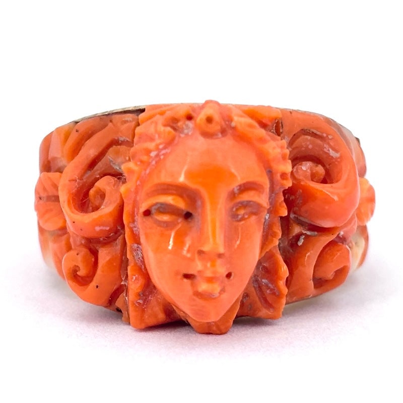 Antique band ring with coral and yellow gold carvings; 11.04 gr.: Artistic and impressive period yellow gold band ring with an enchanting sculptural composition of natural salmon-colored coral, mounted in 18 kt gold. The charm of artistic period jewelry and craftsma