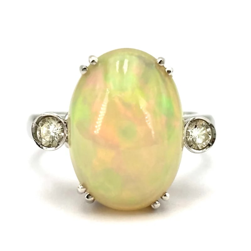 Elegant 18K White Gold Opal Oval Cabochon Vintage Ring with 0.20-0.25ct Diamonds - 7.55g: Elegant vintage-inspired ring in 18K white gold, featuring a luminous oval cabochon opal as the central focal point, accented by refined side diamonds for a soft yet striking contrast. A minimal yet e