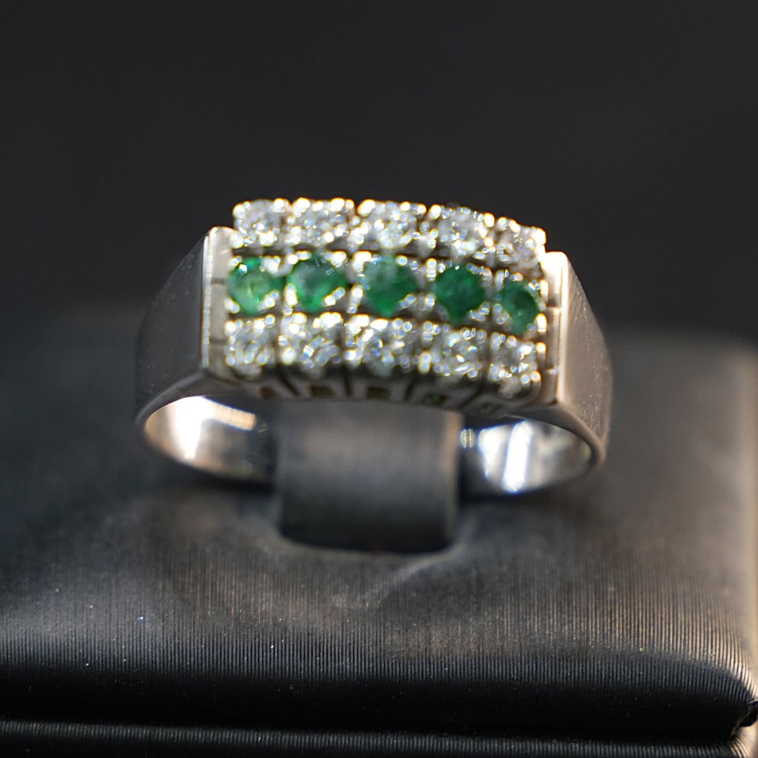 A delicate 18K White Gold Ring with and Row of 5 Small Emeralds and 0.5ct Diamonds, 4.51gr: A delicate ring crafted in 18K white gold, featuring a sparkling diamond accent and a horizontal row of five small emeralds that add vibrant color and elegance. The design emphasizes harmony and refin