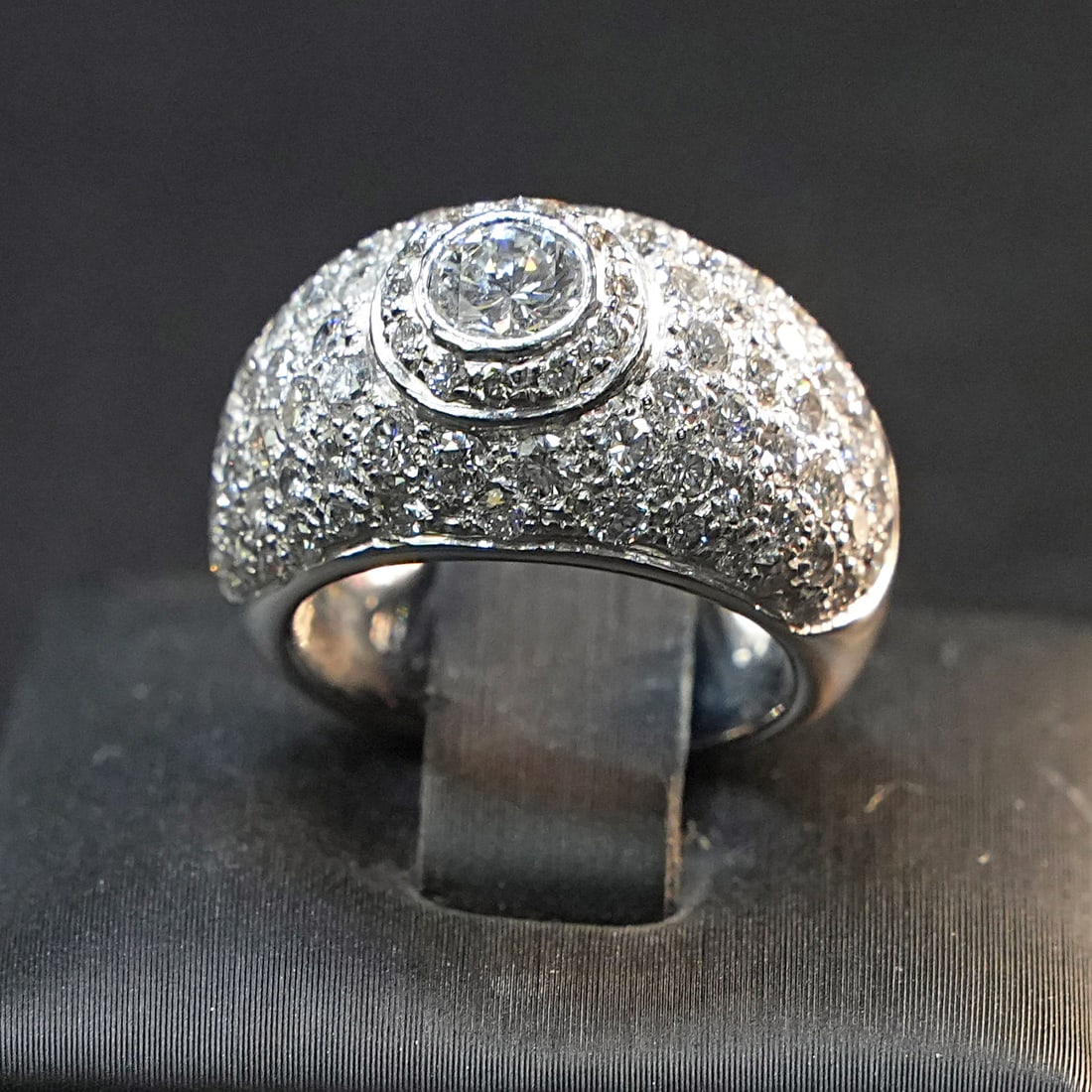 A Central diamond is on this 18kt White Gold Dome Ring with more diamonds 3.44ct total. 0. 11.84 gr: Majestic 18kt white gold Dome ring featuring a prominent central 0.40ct diamond, encircled by 66 smaller diamonds and 20 additional diamonds, for a dazzling, luxurious effect. Its rounded, regal desig