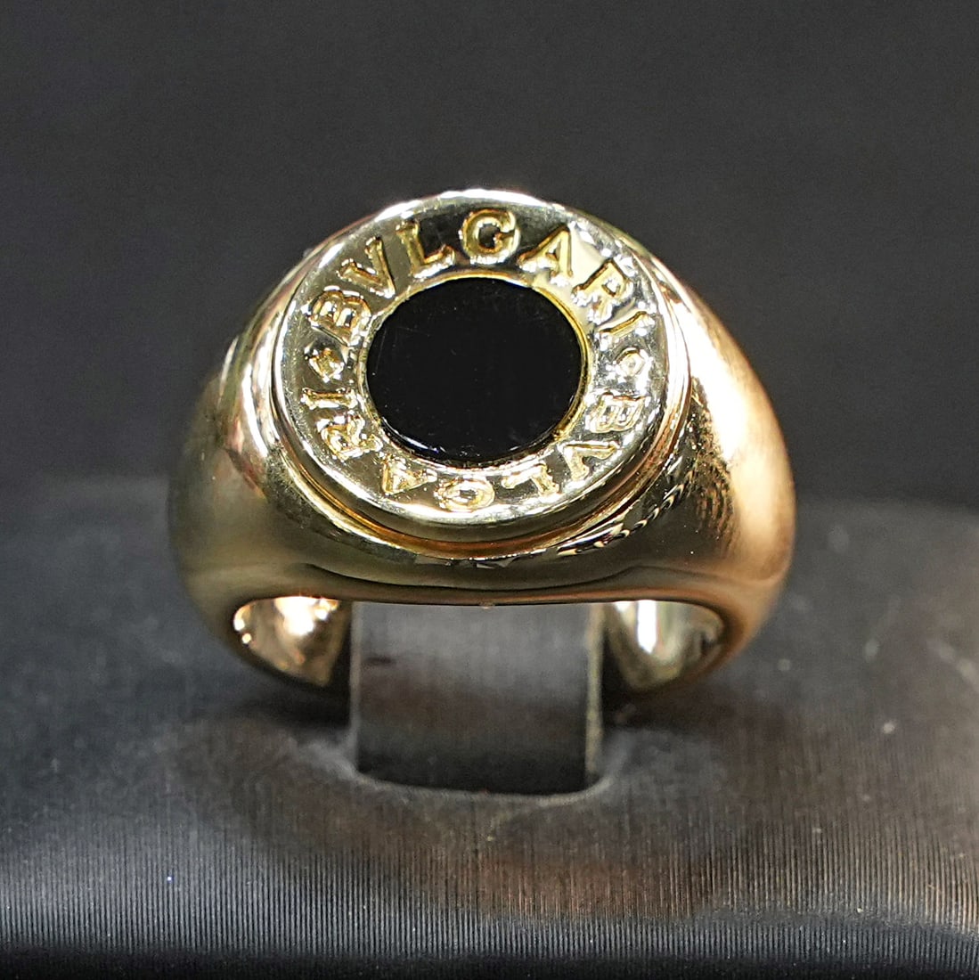Stunning Bulgari Signature 18kt Yellow Gold Chevalier Ring with Deep Onyx Centerpiece, 11.58 gr: Stunning Bulgari 18kt yellow gold Chevalier ring featuring a mesmerizing deep black onyx, framed by the iconic Bulgari signature. The onyx exudes a mysterious, velvety sheen, evoking elegance and stre