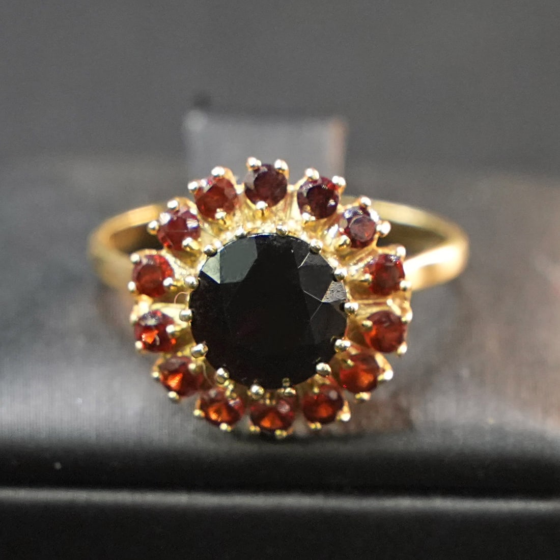 Striking Vintage Garnet Halo Ring in 18K Yellow Gold, 4.06gr: Striking vintage ring crafted in 18K yellow gold, defined by a vivid central garnet embraced by a refined circle of smaller garnets. The composition radiates warmth and depth, offering a bold yet bala