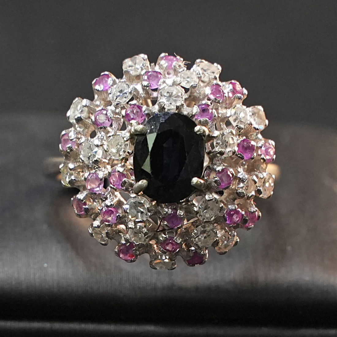 18K White Gold Ring with central Sapphire surrounded by a Rubies and 0.63ct Diamond Halo , 5.93gr: Refined ring crafted in 18K white gold, centered by a vivid sapphire embraced by a luminous halo of rubies and diamonds. The layered setting enhances depth and contrast, creating a sophisticated compo