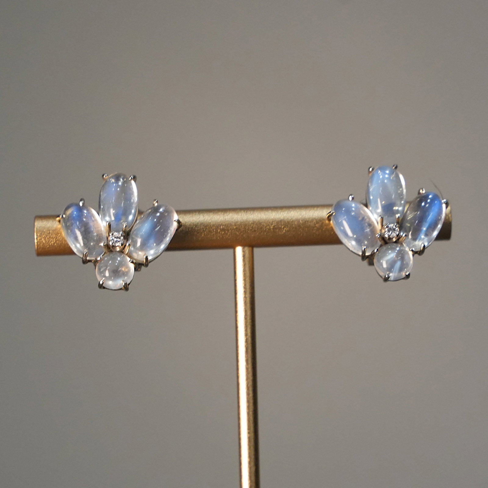 Bouquet-Inspired Moonstone Clip Earrings in 18K White Gold and 2 Diamonds 0.10 ct total, 6.91 gr: Refined clip earrings crafted in solid 18K white gold, featuring a sculpted bouquet-inspired silhouette. The fan-shaped arrangement highlights luminous moonstones with soft bluish reflections, while a