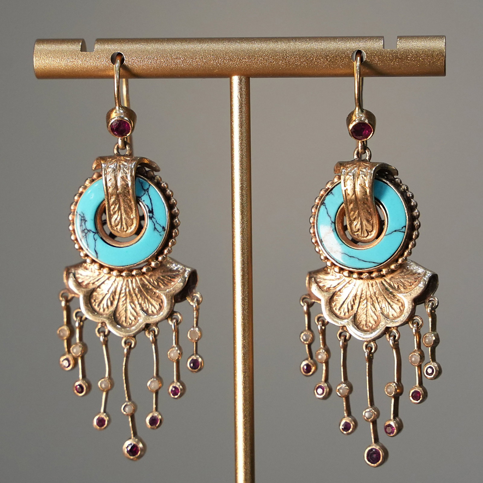 Ethnic Chic Style 14K Yellow Gold Hook Drop Earrings with N. 2 Turquoises and Rubies , 14.69 gr: Striking drop earrings crafted in solid 14K yellow gold, designed with classic hook fittings and an eclectic ethnic-chic inspiration. The composition blends ancestral motifs with refined handwork, fea