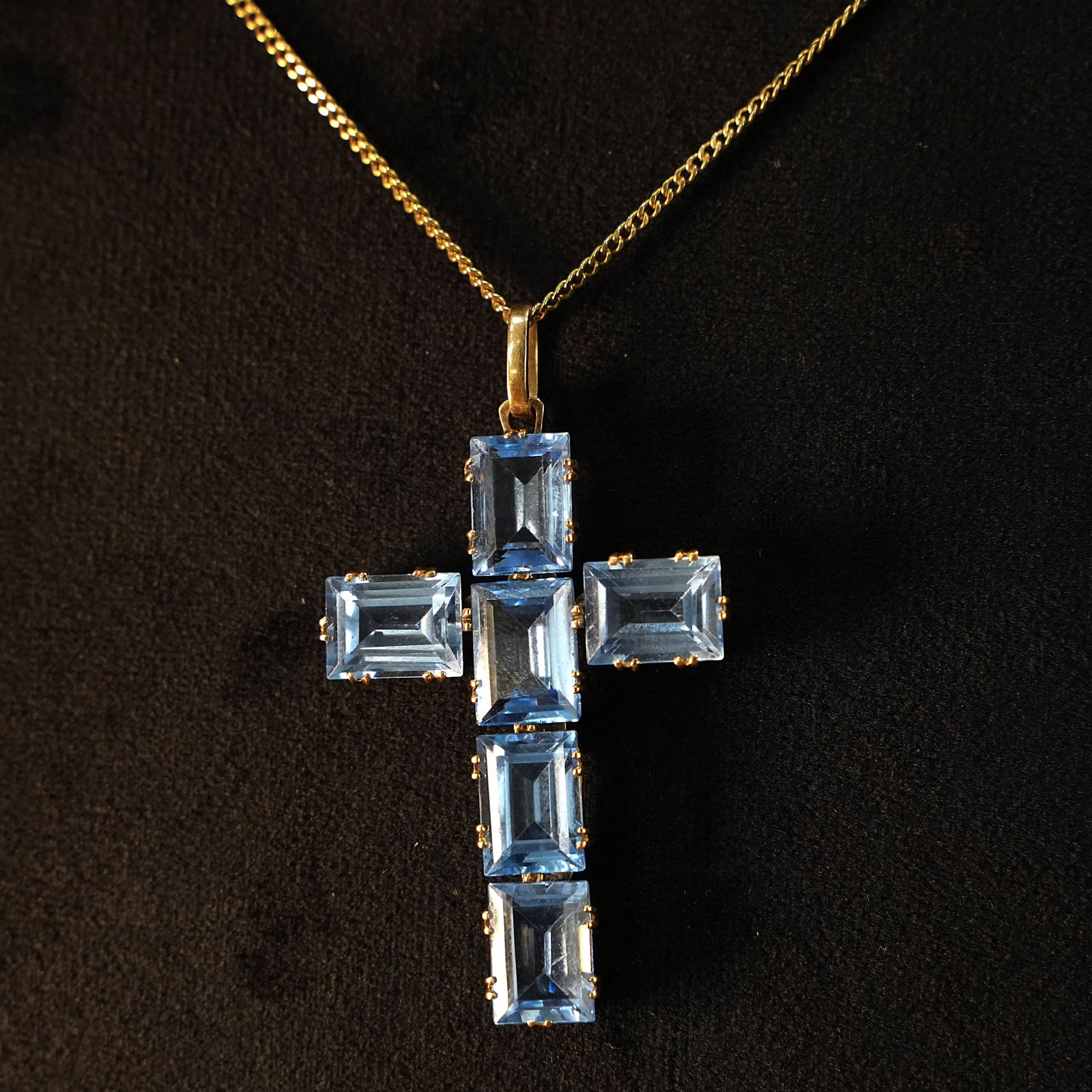 Radiant 18kt Yellow Gold Cross Pendant Adorned with Six Blue Quartz Stones, 10.28gr: Radiant 18kt yellow gold cross pendant featuring a polished structure with six vivid blue quartz stones elegantly set along the arms, offering a serene and luminous charm. A timeless piece that combin