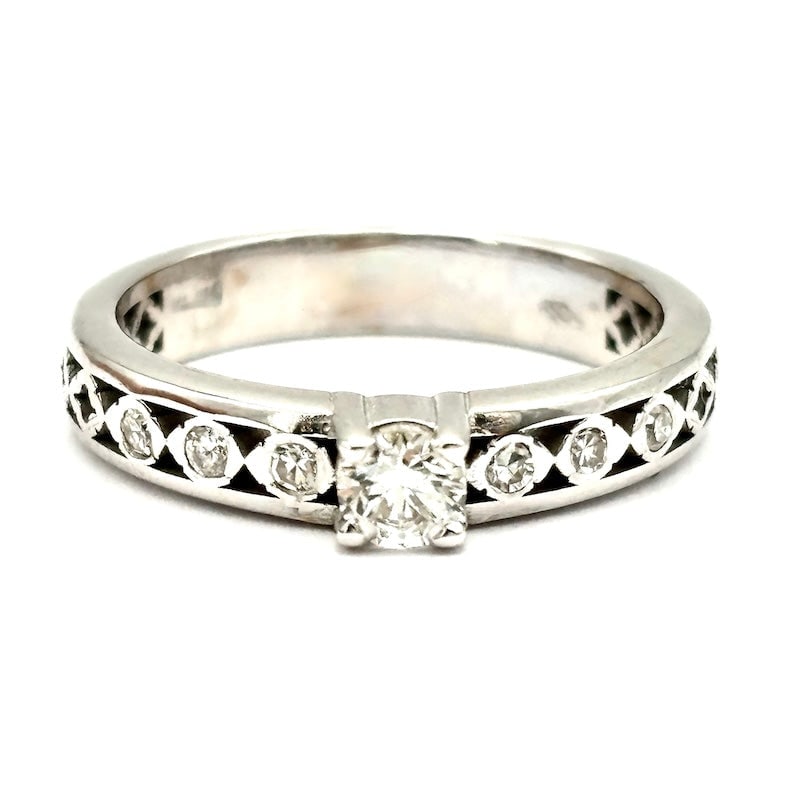 Riviera band ring with solitaire, white gold and diamonds; 3.19 gr: Magnificent 18 kt white gold band/riviera ring with central 16-point solitaire diamond. Linear and luminous design for an exclusive, luminescent and super feminine piece of jewelry. Our company's cert