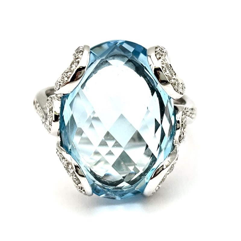 Oval blue topaz and brilliants ring, white gold; 12.69 gr.: An enchanting and youthful touch of blue! Ring with intense blue topaz oval and patterned side waves of brilliants, on 18 kt white gold. A light blue jewel and fresh from the bargain! Our company's ce