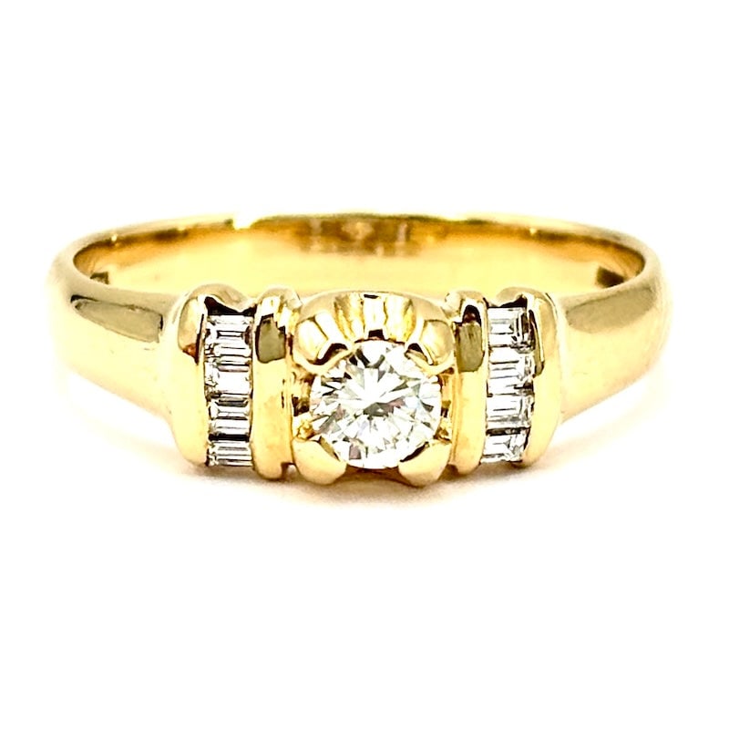 Yellow gold ring with solitaire brilliant and baguettes; 3.60 gr.: Exquisite, romantic 18 kt yellow gold band ring, with central 15-20 point solitaire brilliant-cut diamond and with rails of additional baguette-cut diamonds on the sides. A ring as vexatious, precious