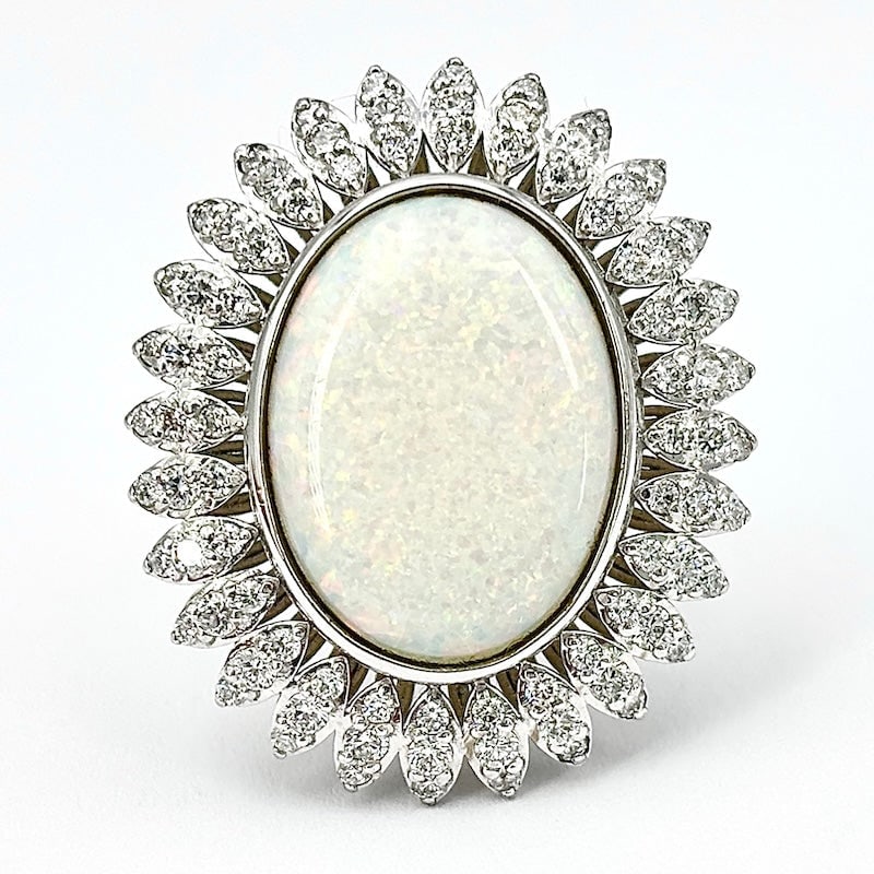 Opal, brilliants and gold maxi daisy ring; 13.28 gr.: A gemstone unique in the mineral world is the star of this sophisticated and impressive piece of jewelry! Maxi daisy ring with oval cabochon opal, iridescent, romantically framed by rich petals of bri