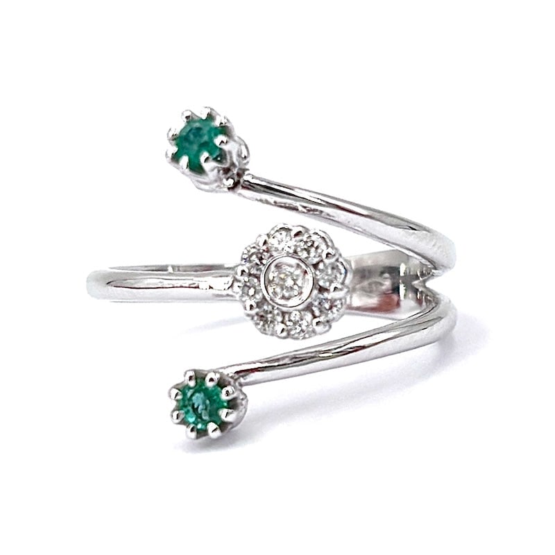 Contrarie ring flower brilliants, emeralds, white gold; 3.67 gr.: A set of essential and sinuous lines design a contrarie ring with a flower of brilliants and double emerald, extremely refined and incredibly feminine. A minimal and very classy ring offered at a pric
