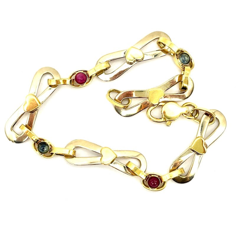 Two-tone gold flakes chain bracelet, sapphires and rubies; 13.5 gr - 19.5 cm: A romantic, feminine, vexatious, two-tone 18 kt gold bow chain bracelet with small hearts and small sapphires and rubies for 0.40-0.50 ct total, round cabochon cut. Reconditioned to new. Our company's