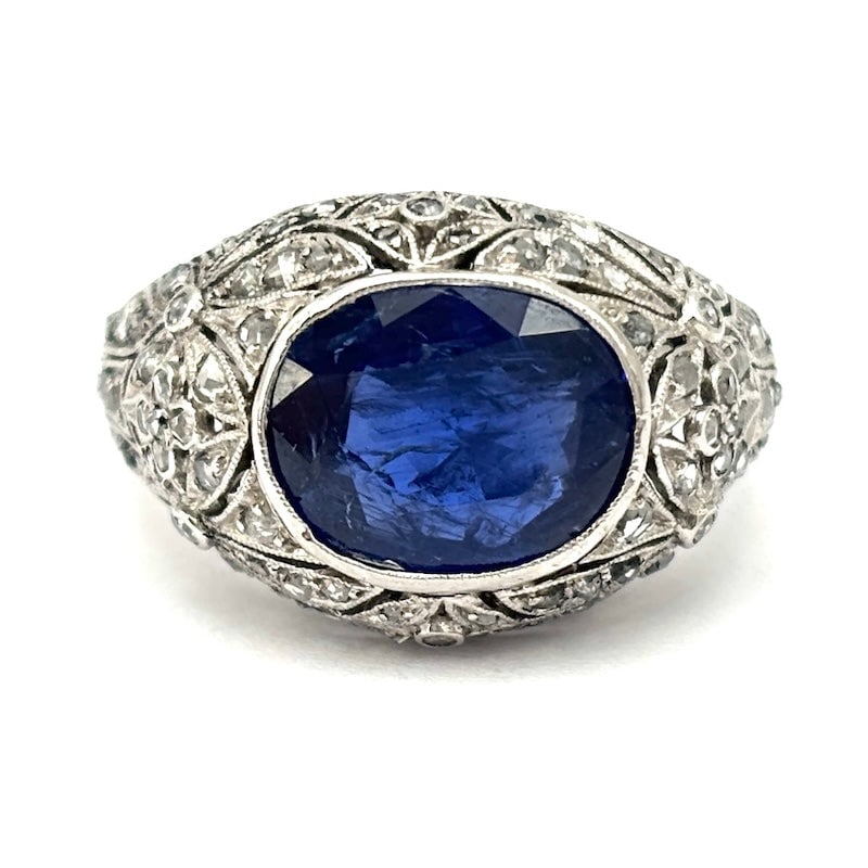 Vintage sapphire and diamond ring on openwork gold; 5.32 gr: A unique piece of old-school fine jewelry! A finely pierced white gold signet ring with dense diamonds, featuring a romantic and masterful design that houses a large, faceted oval-cut sapphire. A stun
