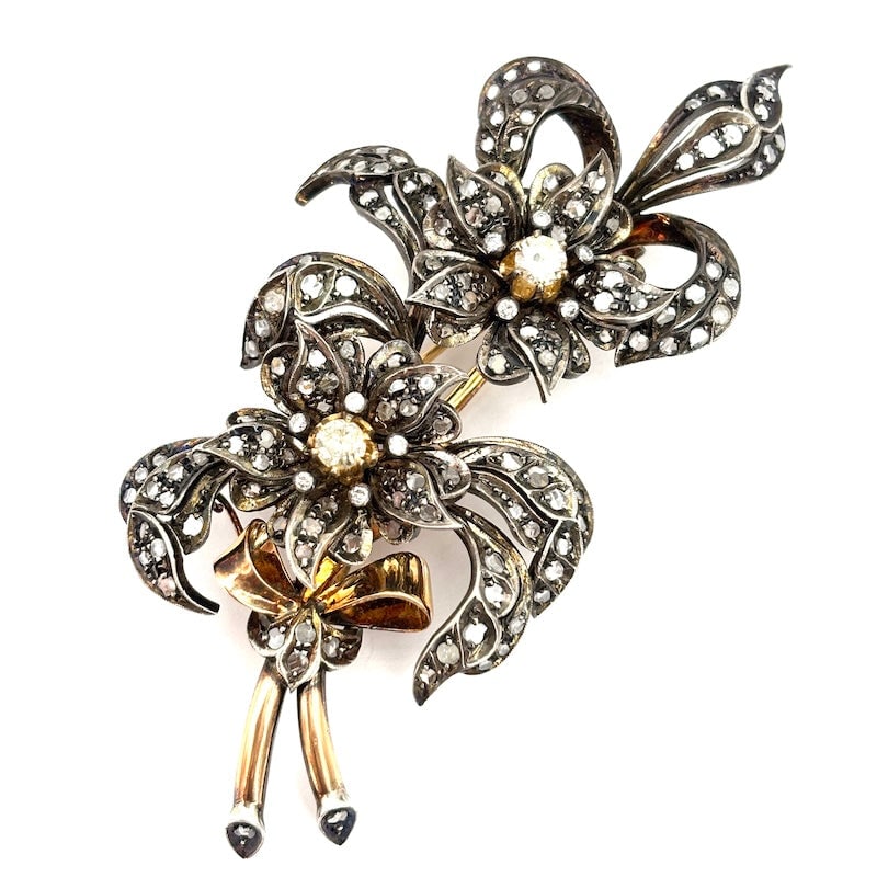 A masterpiece brooch from the late 19th-early 20th century, featuring a floral design, gold, silver,: Disruptive and masterful late 19th-early 20th century period brooch, draped with 2 splendid flowers with large central old-cut solitaires and bows and foliage, excellently crafted in 18 kt gold, with 