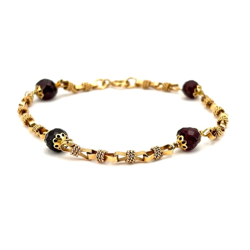 Vintage garnet and gold bracelet; 11.37 gr: Charismatic and sophisticated vintage bracelet in retro style, with irregular faceted garnet grains intertwined in 18kt yellow gold, with iconic flower caps and bow inserts, cords, and gold chain. An 