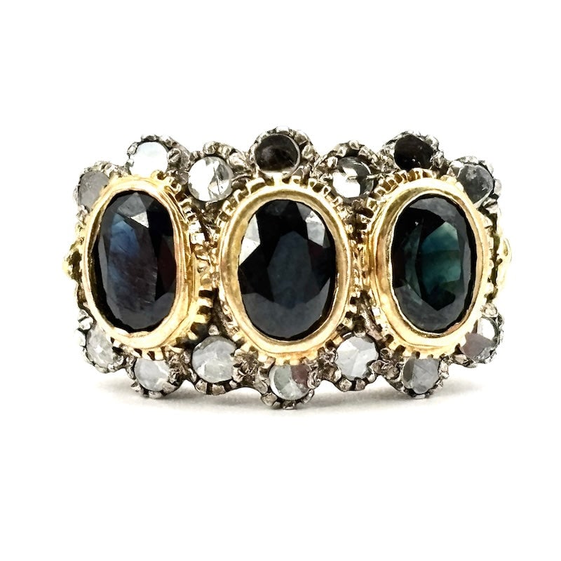 Vintage antique-style sapphire and diamond trilogy ring; 6.06 gr: Poetic proposal for a vintage 1950s-1960s trilogy ring with an old-fashioned design! Fascinating antique-style ring in yellow gold with three sapphires and perimeter diamonds, set in silver. The retro