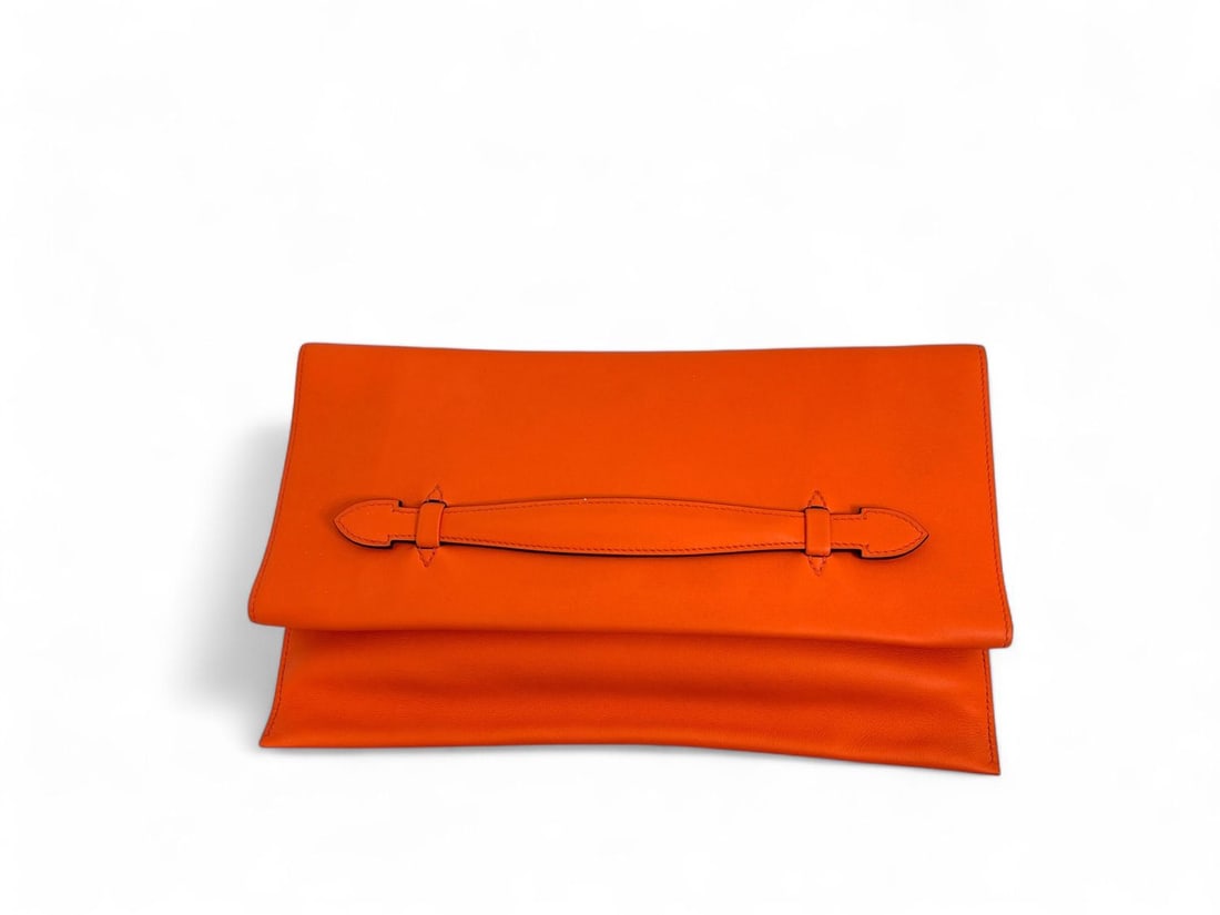 Hermes Orange Leather Pliplat Clutch: Hermes Pliplat, an architectural masterpiece of design that can be elegantly folded or carried as a grand clutch. Crafted in the iconic Hermes Orange leather, its minimalist and ingenious structure re