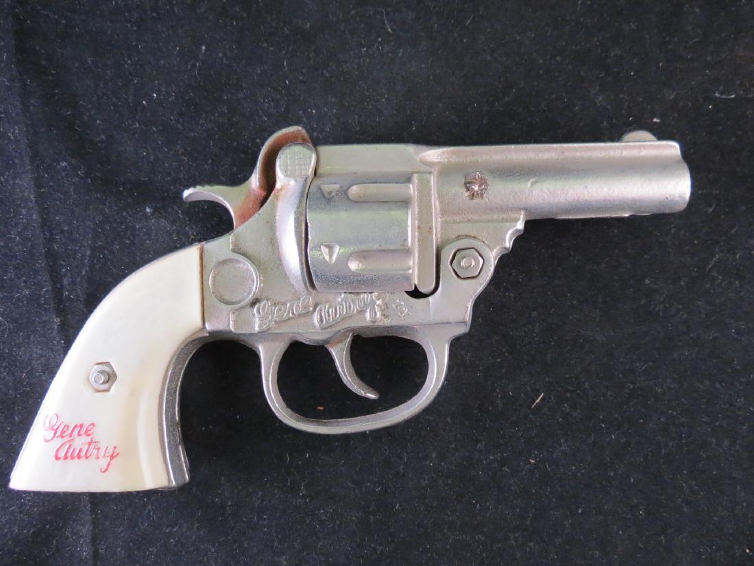 Vintage Gene Autry Endorsed Cap Gun: Gene Autry in raised letters on the metal body and in script on the plastic handles. It works fine when you pull the trigger, but you have to manually reset the trigger afterward. 6.5 inches long. Cos
