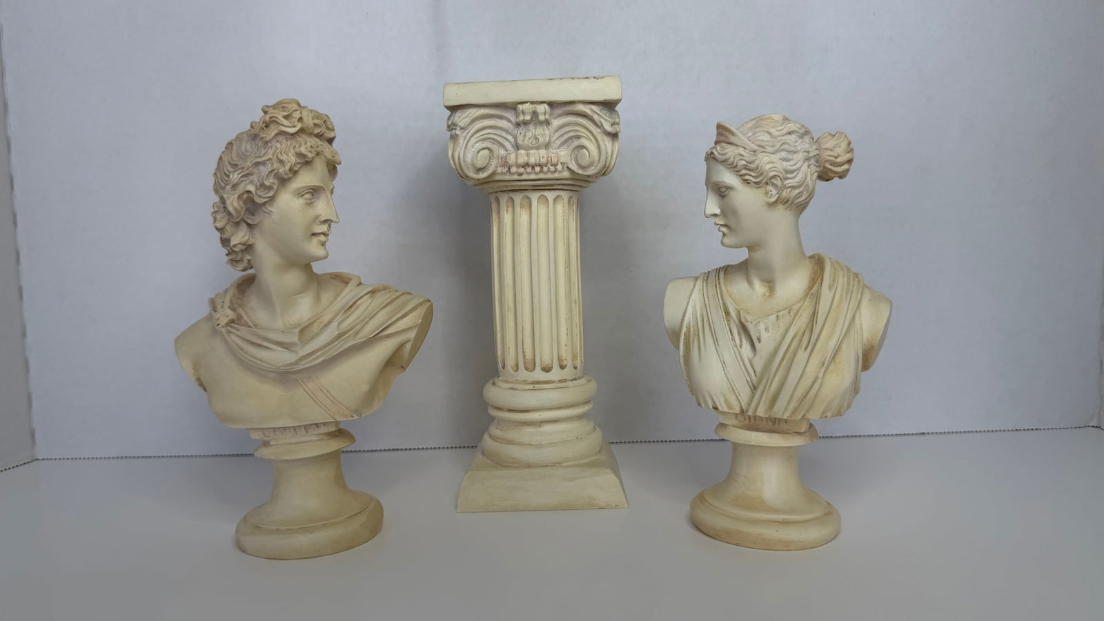 Classical Greco-Roman Bust Set: Apollo, Artemis & Ionic Column (Made in Greece): An elegant three-piece decorative set celebrating the aesthetic ideals of classical antiquity, featuring finely cast busts of Apollo and Artemis, paired with a miniature Ionic column pedestal.