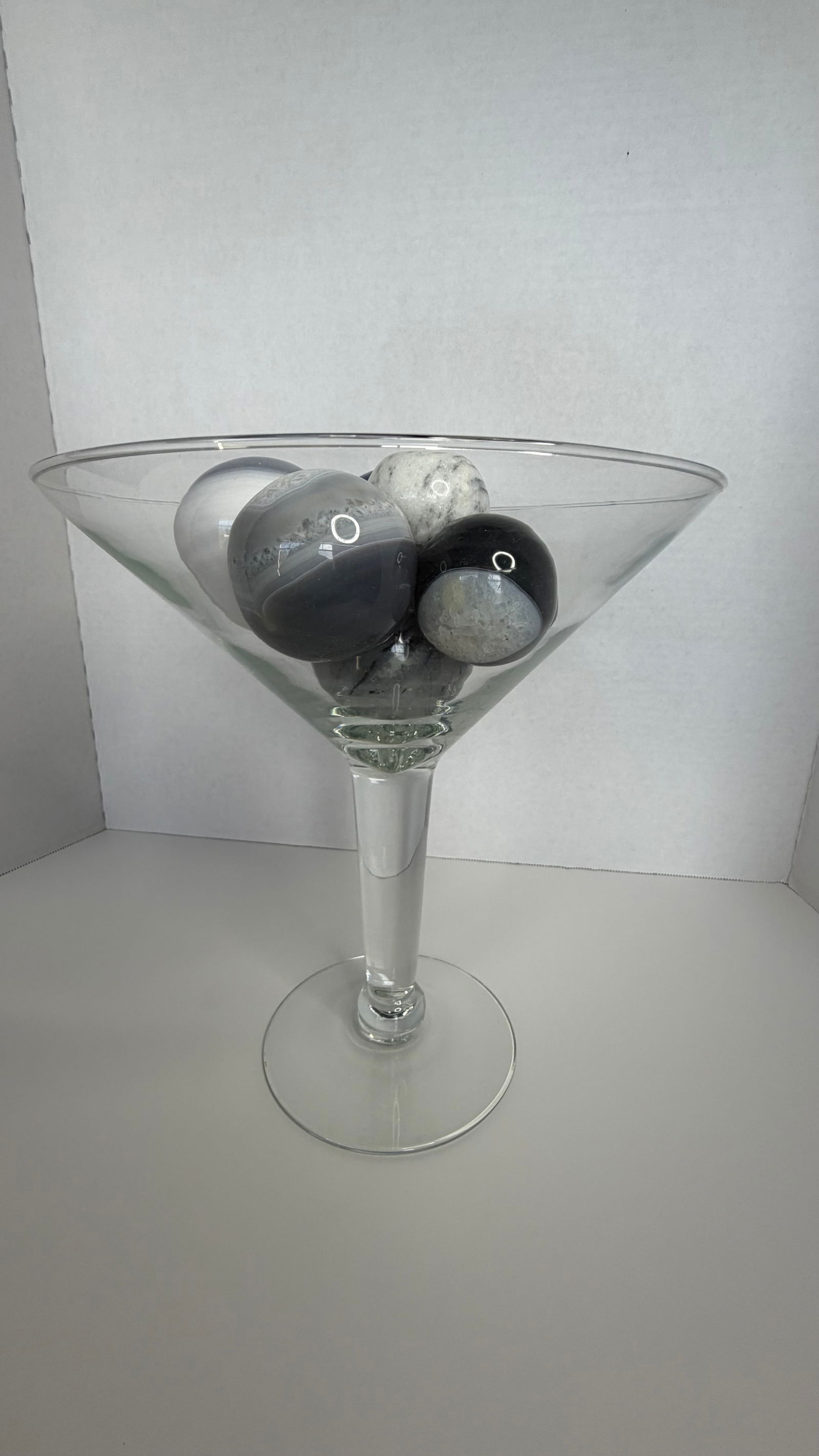 Decorative Oversized Martini Glass with Polished Brazilian Stone Spheres (8-Piece Set): A contemporary decorative arrangement featuring an oversized clear martini-style glass filled with seven polished semi-precious Brazilian stone spheres. The spheres, presented in harmonious tones of