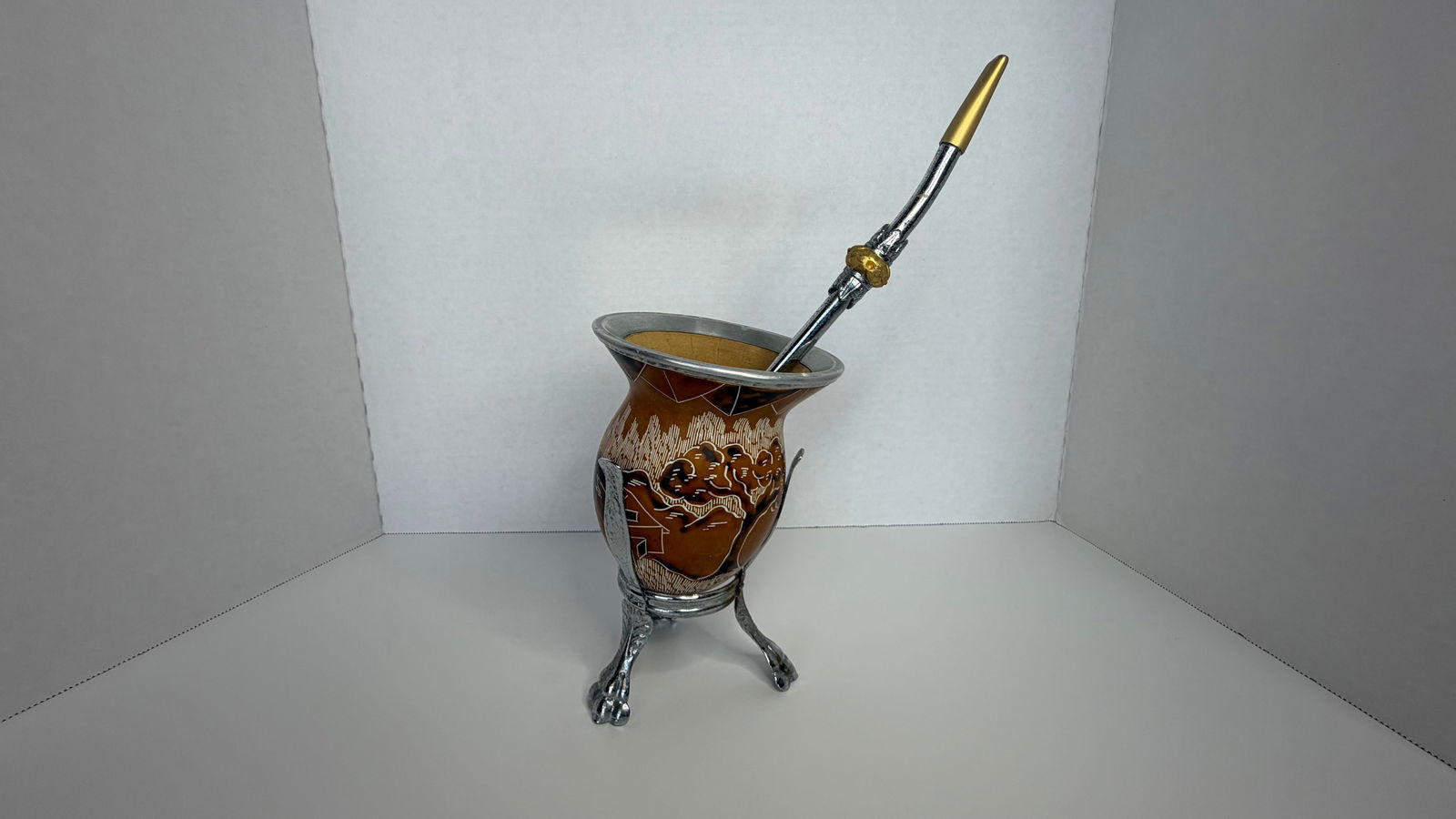 Traditional Brazilian Mate Gourd with Bombilla and Ornate Stand: A finely handcrafted traditional mate gourd set from Brazil, comprising a natural gourd cup with engraved detailing, an ornate aluminum stand, and a classic metal bombilla for sipping. The gourd featu