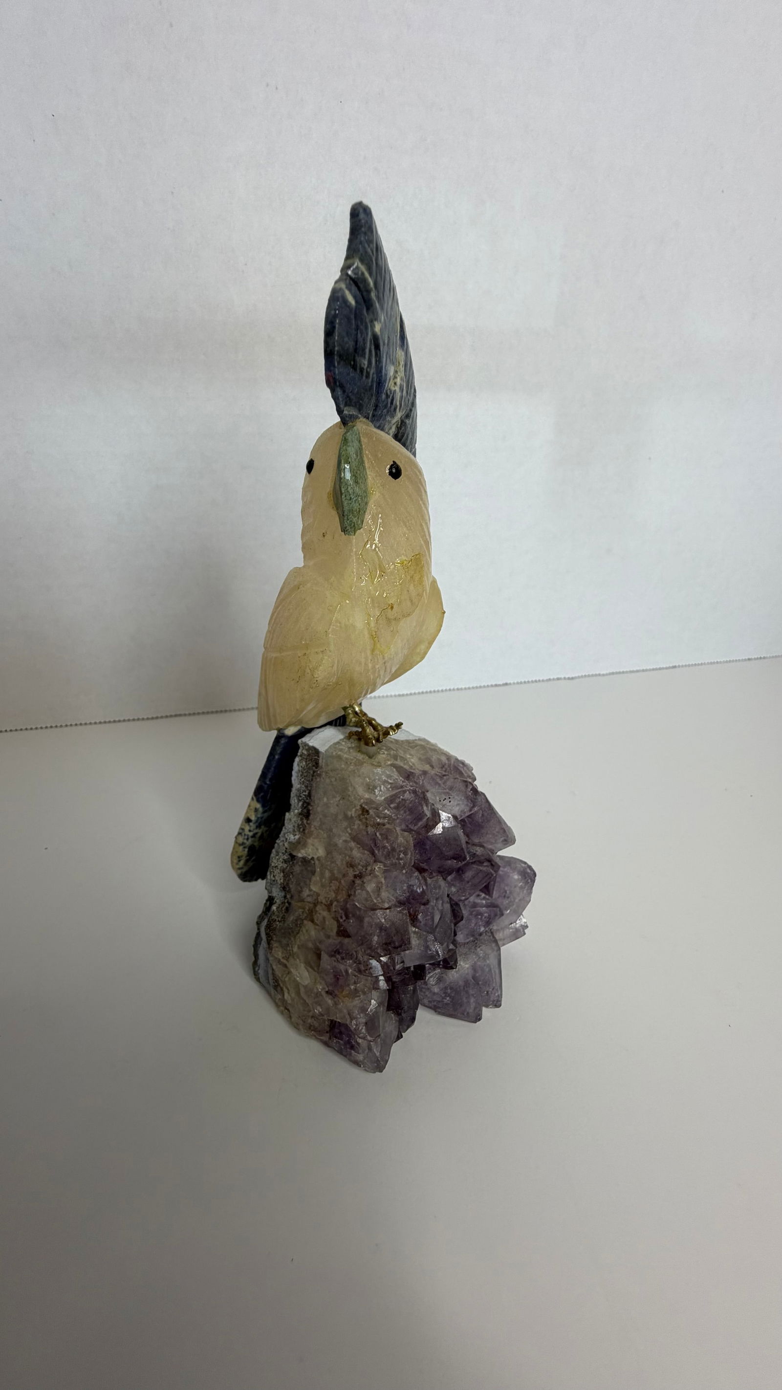 Gemstone Cockatoo Sculpture on Amethyst Crystal Base: A majestic Brazilian gemstone sculpture of a cockatoo, perched on a glittering cluster of natural amethyst crystals, radiating both elegance and exotic charm. This piece exemplifies the harmony of min