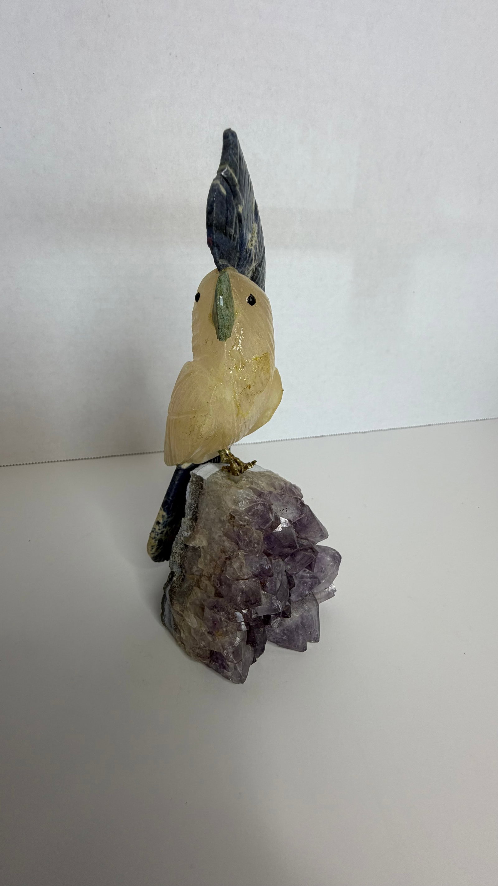 Gemstone Cockatoo Sculpture on Amethyst Crystal Base: A majestic Brazilian gemstone sculpture of a cockatoo, perched on a glittering cluster of natural amethyst crystals, radiating both elegance and exotic charm. This piece exemplifies the harmony of min