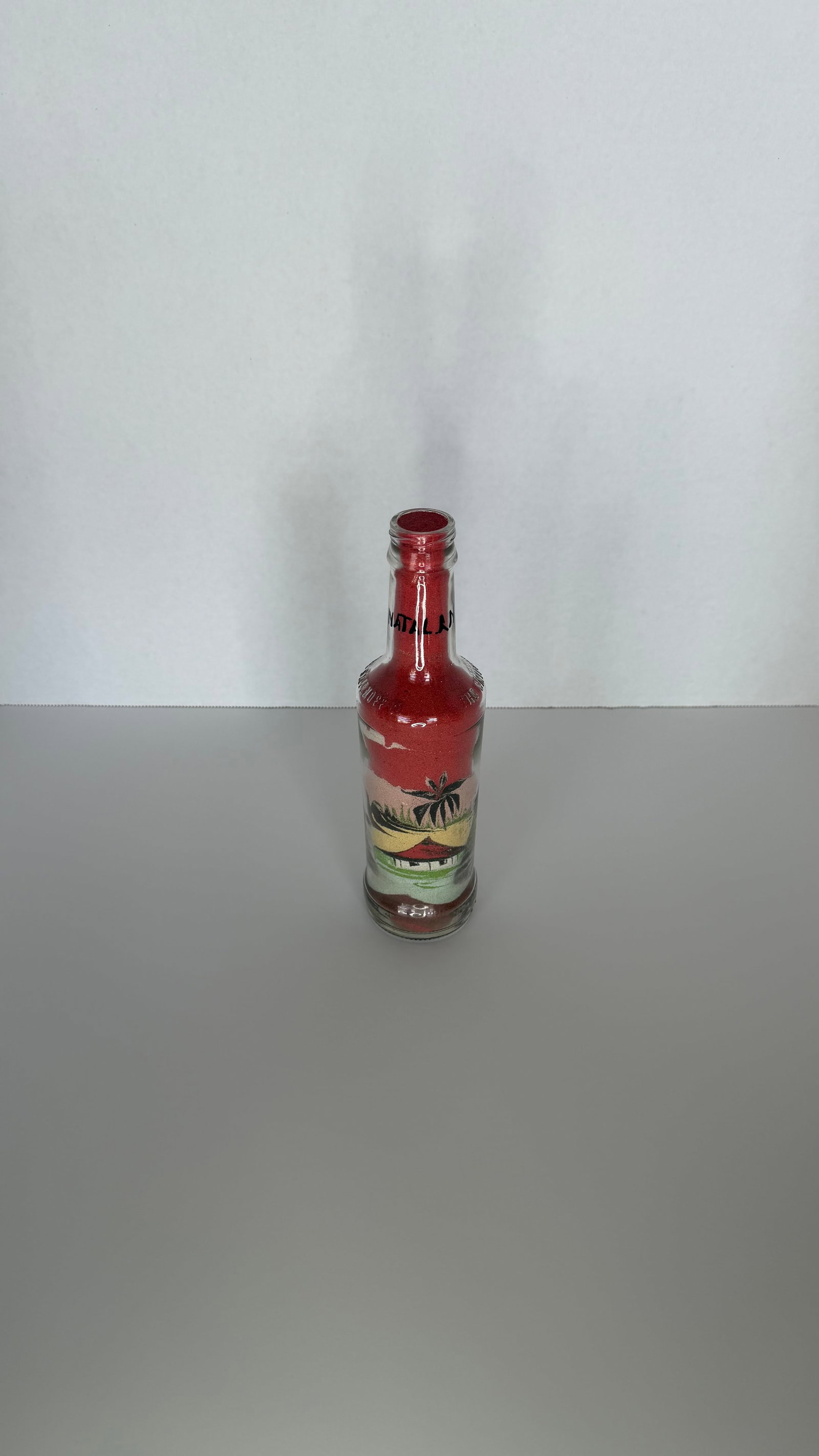 Handcrafted Sand Art Bottle with Tropical Sunset Landscape: A meticulously crafted glass bottle containing a vibrant sand art scene, showcasing remarkable detail and control. Layers of colored sand have been skillfully poured to depict a tropical landscape, co