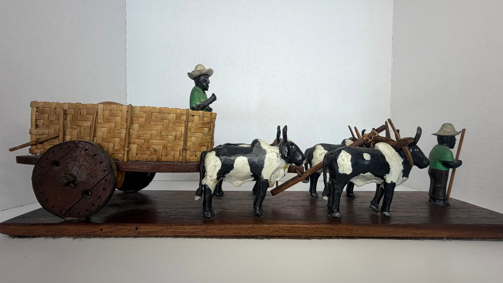Handcrafted Folk Art Ox Cart Sculpture | Early to Mid-20th Century | Latin American Origin: This richly detailed folk art sculpture depicts a traditional ox-cart scene, handcrafted with remarkable care and charm. Featuring six yoked oxen and two peasant figures; one seated within a woven car