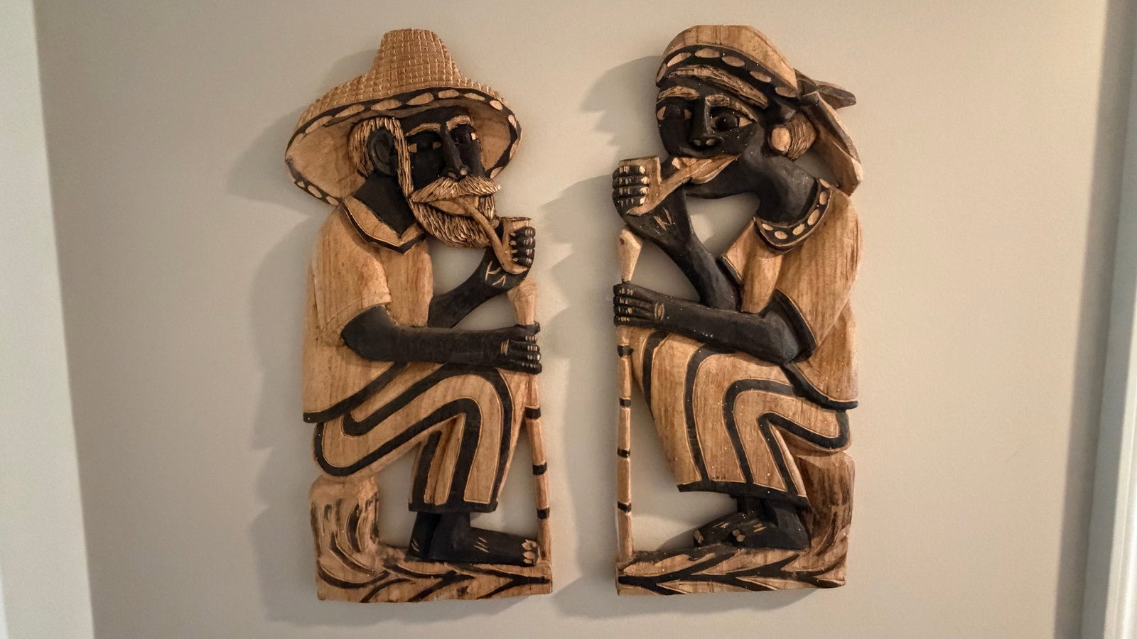 Pair of hand-carved wooden wall sculptures of a man and woman seated in contemplative poses: These wooden carvings are beautifully stylized depictions of a man and a woman in a seated posture, possibly engaged in a shared ritual or moment of reflection.Materials & Style:Medium: Carved wood wi