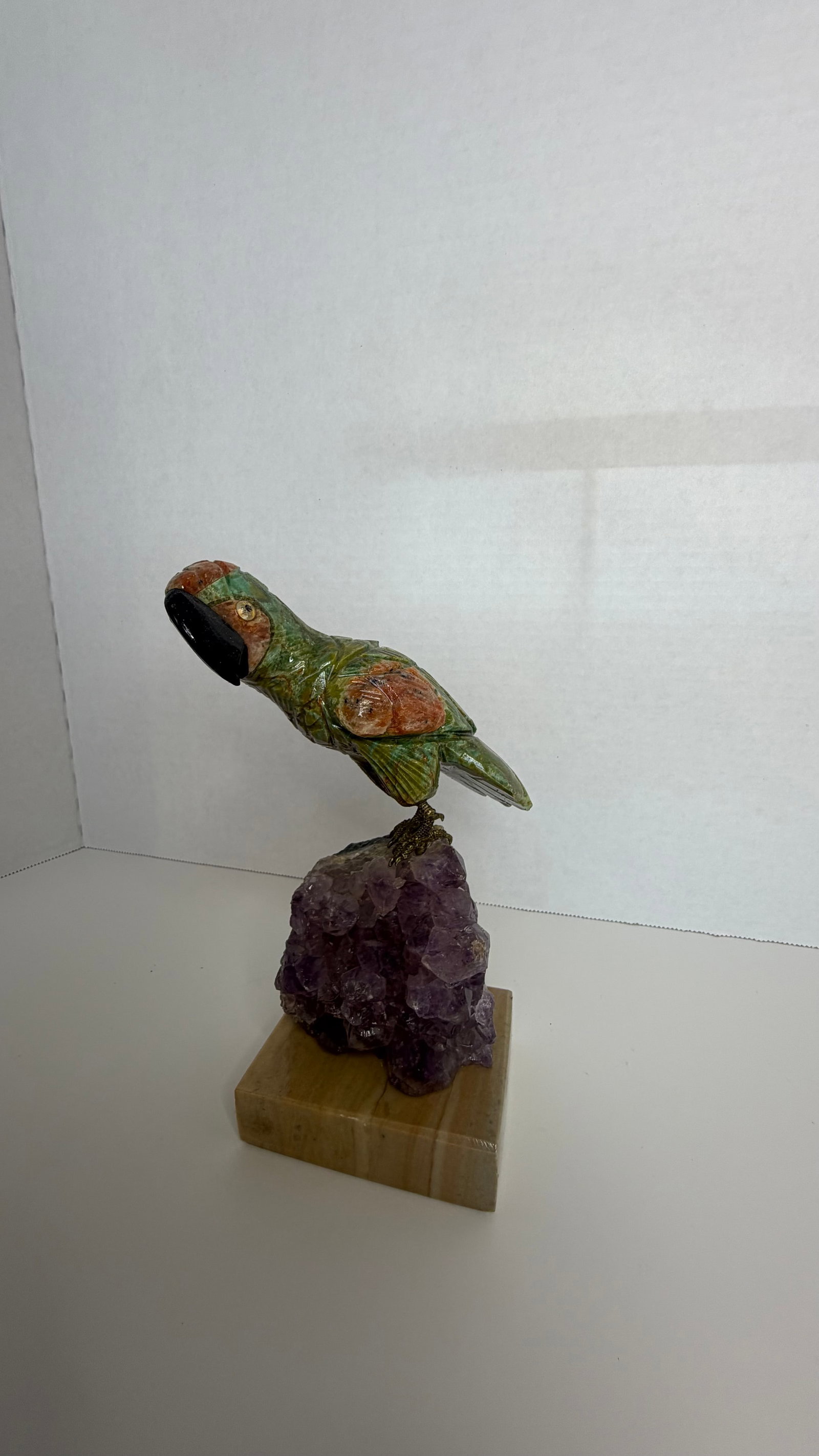 Hand-Carved Gemstone Parrot on Amethyst Cluster: A stunning and vibrant example of Brazilian gemstone artistry, this hand-carved parrot sculpture is perched atop a radiant amethyst crystal cluster, blending natural mineral beauty with lifelike