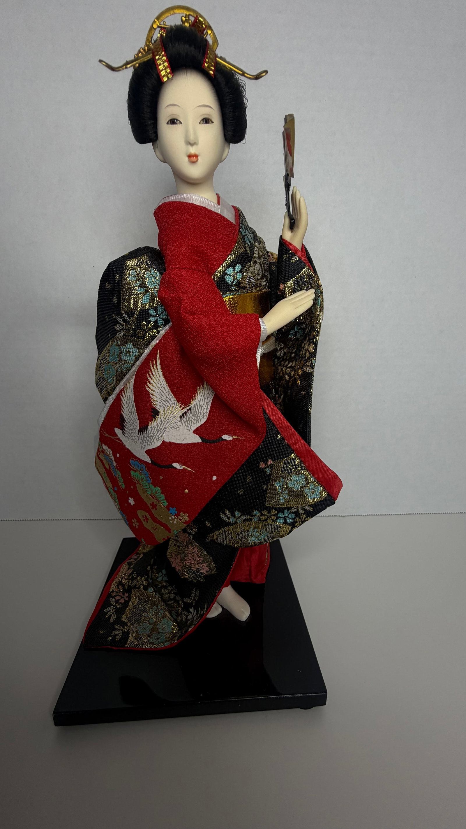Traditional Japanese Geisha Doll in Brocade Kimono with Fan (Sensu): A refined and intricately detailed handcrafted Japanese Geisha doll, dressed in an exquisite, multi-layered formal kimono of richly patterned gold, red, and black brocade. Poised in a graceful