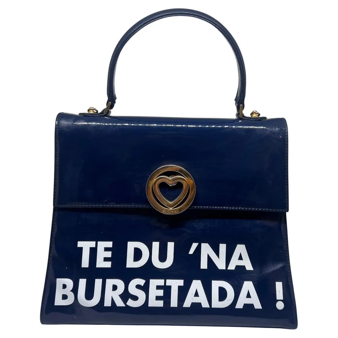 A 1980s Iconic Blue and White Handbag by Franco Moschino " Te du na bursetada! ": This piece exemplifies Moschino's characteristic sense of humor and playful approach to fashion. The bag is a structured, dark blue plastic handbag with a top handle. It has a bold statement printed i
