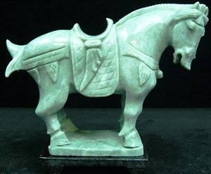 REAL JADE SADDLED TANG HORSE: L: 7", W: 3", H: 6". This horse is made from one piece solid Taiwan jade. It appears light green with some area dark green. It comes with a wooden base