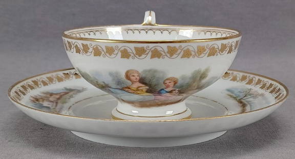 Sevres Hand Painted Watteau Scene Tea Cup & Saucer: Antique footed porcelain tea cup and saucer. Decorated with a hand painted Watteau scene with two ladies on the cup. The saucer has hand painted landscape scenes on either side. Gold ivy leaf band