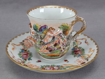 Antique Capodimonte Style Demitasse Cup & Saucer A: Nice antique late 19th century German Capodimonte style porcelain cup and saucer. With relief molded and hand painted Neoclassical scenes on the cup and cherubs with rose swags on the saucer. The cup