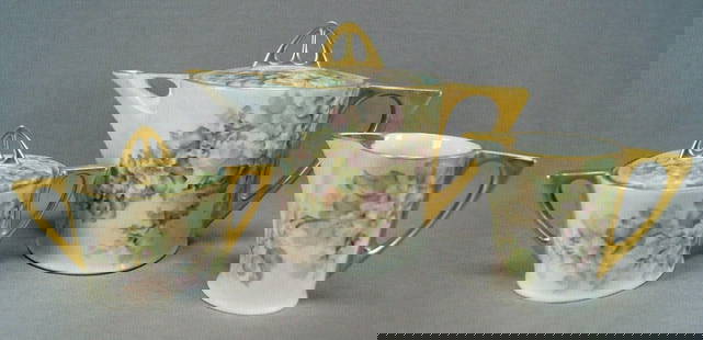 Hutschenreuther Hand Painted Tea Trio: Porcelain tea trio including teapot, creamer, and sugar in an Art Deco shape. Each piece is decorated with hand painted pink and white flowers. With gold gilding along the rim and to handles, spouts,