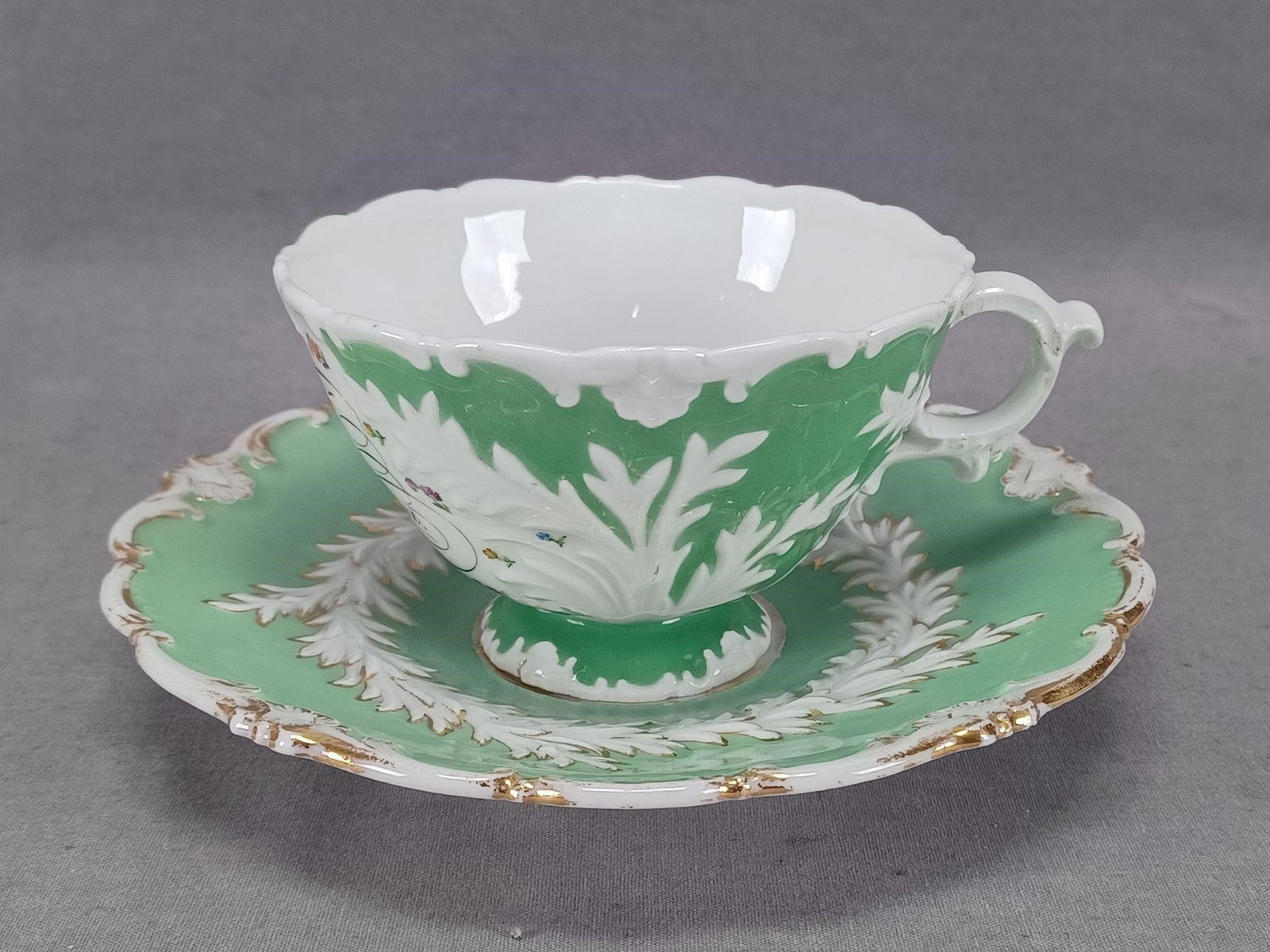 Meissen Zum Andenken Tea Cup & Saucer C.1831-1860: Antique German porcelain cup and saucer. Beidermeier period with relief molded leaves and scrollwork with gold highlights. Has a green background. The cup says "Zu Anderken" in black script which tran