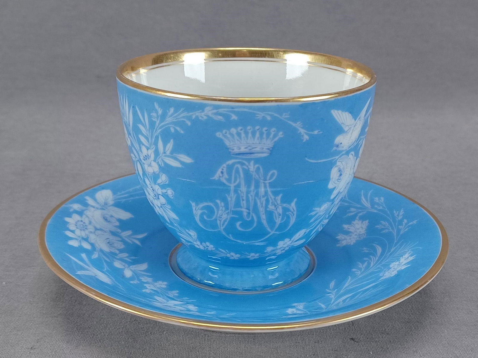 KPM Berlin MP Monogram Blue Cup & Saucer: Antique late 19th century German porcelain tea cup and saucer. Decorated in blue. The cup has a white crown above a scripted MP monogram with white bird, dragonfly, and flowers. The saucer is decorate