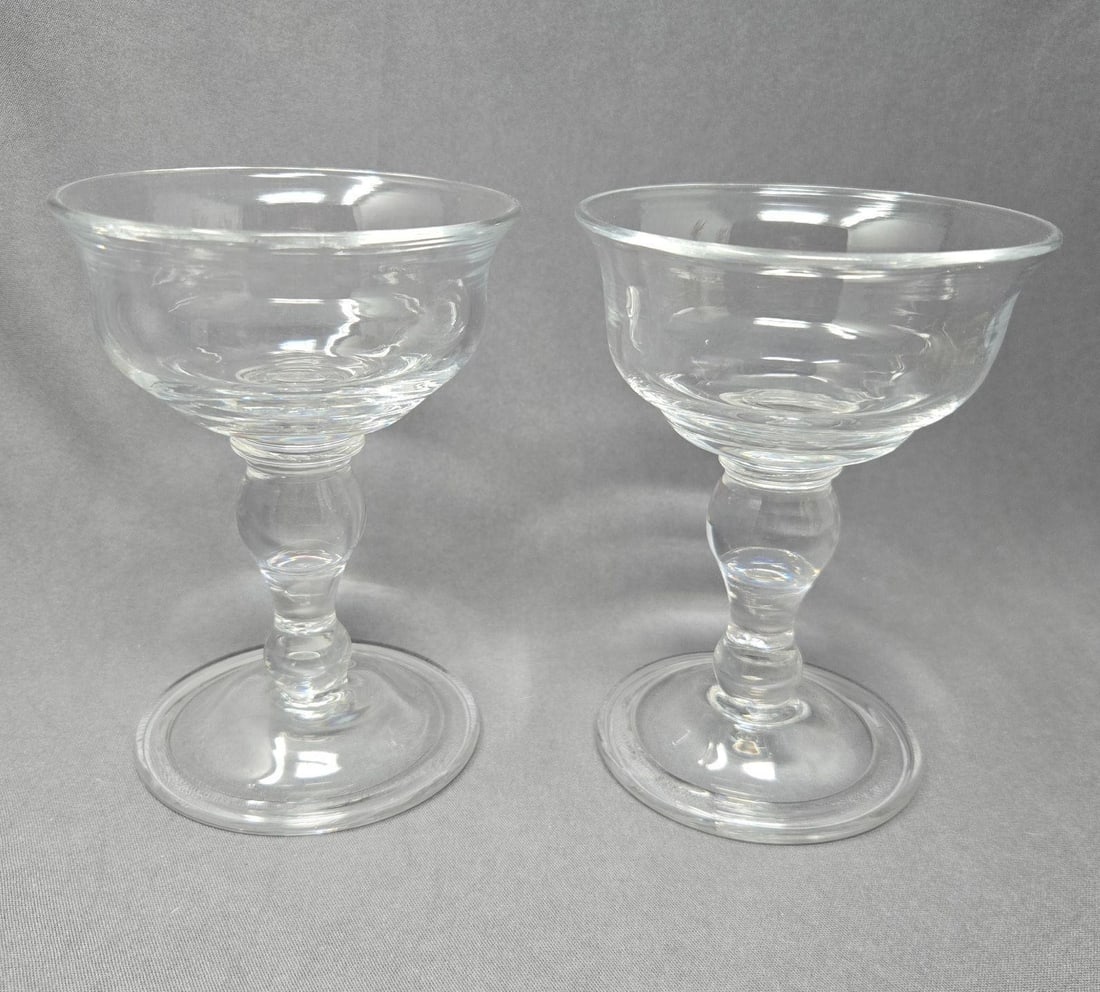 2 Williamsburg Royal Leerban Champagne Glasses: Set two excellent condition Williamsburg Restoration Baluster Stem Champagne / Sherbet Glasses. Measures 5 inches tall and 3 3/4 inches in diameter. No chips or cracks or scratches. Rough pontil mark