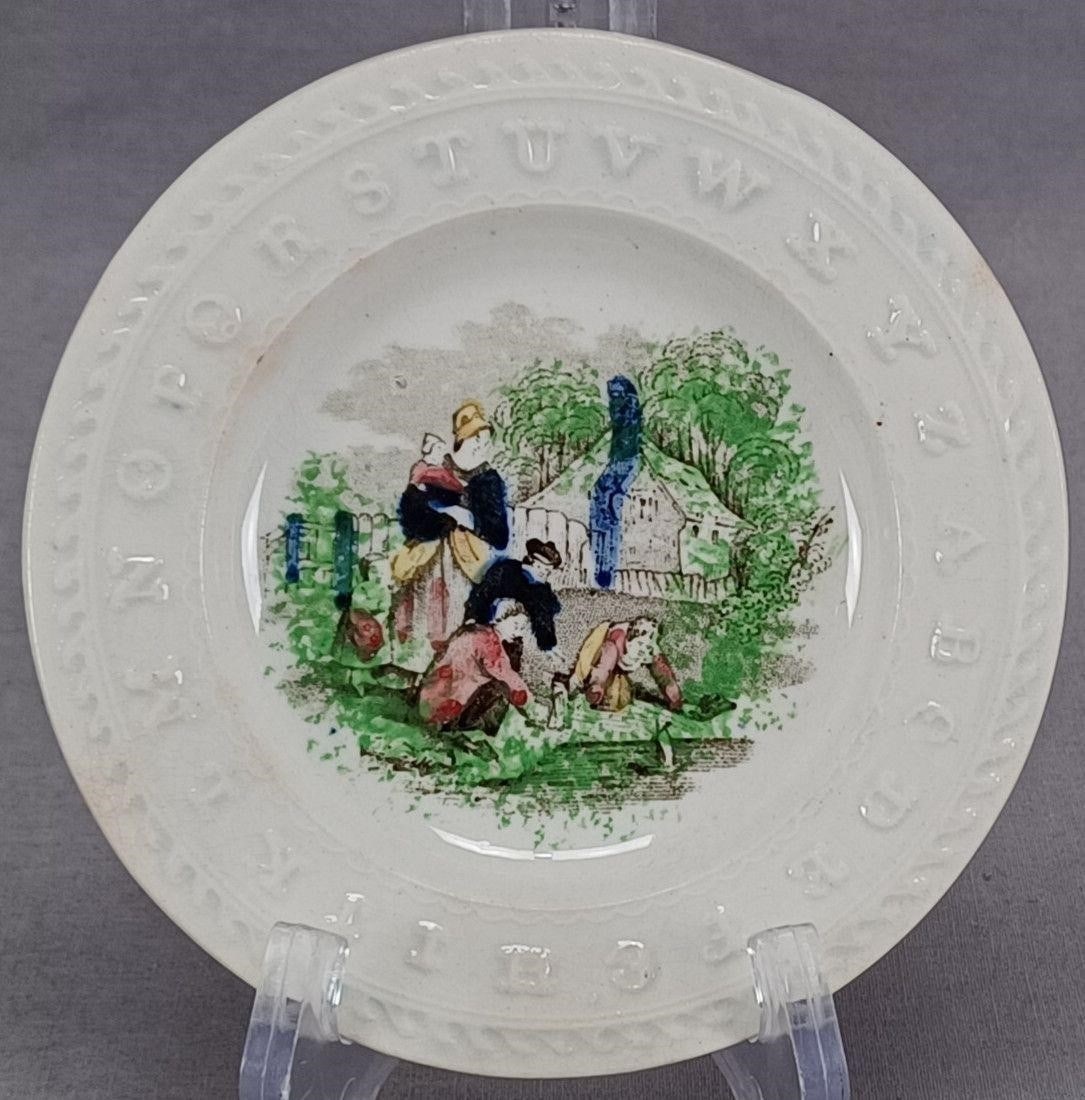 Staffordshire Playing With Boats ABC Plate: Antique British earthenware plate with relief molded ABC border. Decorated with a black transfer scene depicting a woman holding a baby and children playing with boats. With hand colored highlights in