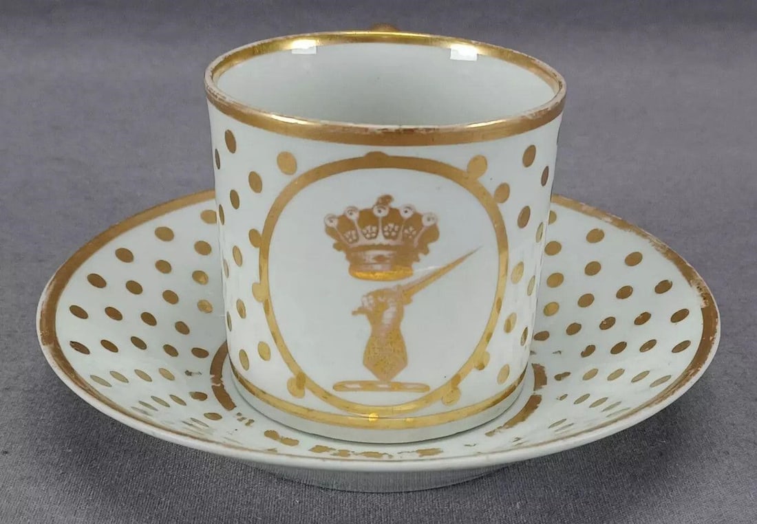 Derby Earl Of Darlington Crest Coffee Can & Saucer: Antique British porcelain coffee can and saucer. Decorated with an armorial crest of a crown above a hand holding a dagger in gold gilding This appears to be the crest of the Earls of Darlington, The